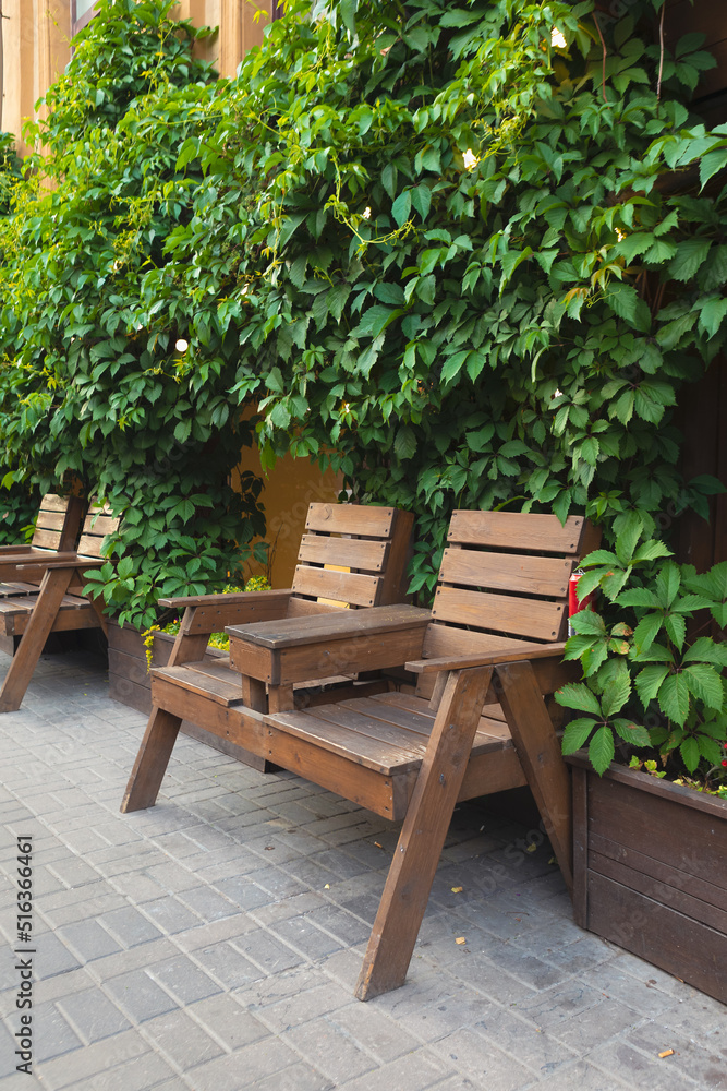 Wood bench in the bushes. Wood chairs with table in front of cafe. Wood bench in the bushes. Wood chairs with table in front of cafe.