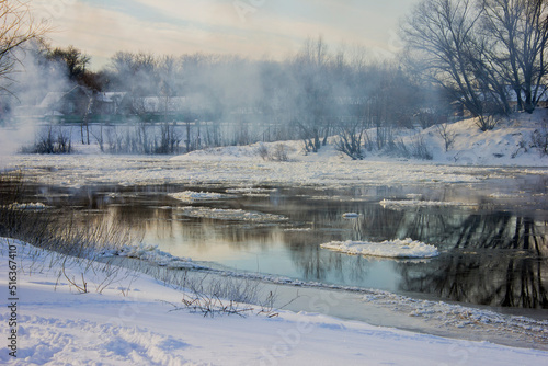 ice drift on a river with snow-covered banks and haze in winter