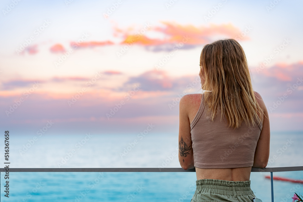 Obraz premium Beautiful young woman standing and looking at the sea and sky