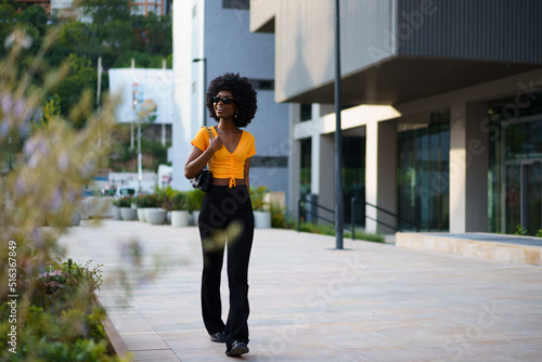 Photo of a stylish young black woman with curly hair wearing orange crop top walking in the street © fotofabrika