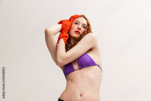 Portrait of attractive young red-haired woman posing in swimming suit top and rubber gloves isolated on grey studio background