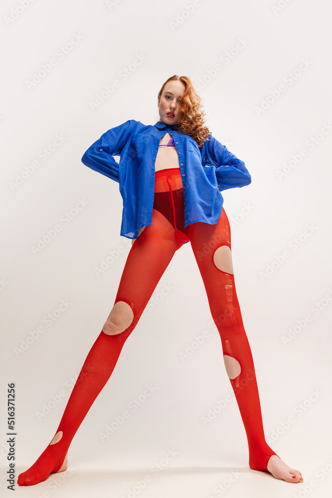 Portrait of beautiful young girl in blue shirt and red torn tights posing isolated over grey studio background. Extraordinary, weird look Portrait of beautiful young girl in blue shirt and red torn tights posing isolated over grey studio background. Extraordinary, weird look