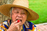 An Asian grandmother is eating a small tomato