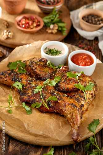 Traditional georgian dish - chicken tabaka on wooden background in rustic style. Roasted whole chicken in georgian style on wooden table. Chicken tabaka with sauces in rustic style.