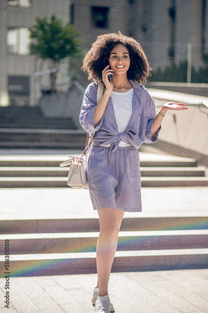 Pretty curly-haired woman walking in the street and talking on the phone