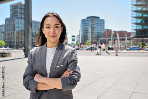 Fotografie Young confident smiling Asian business woman standing on busy street, portrait
