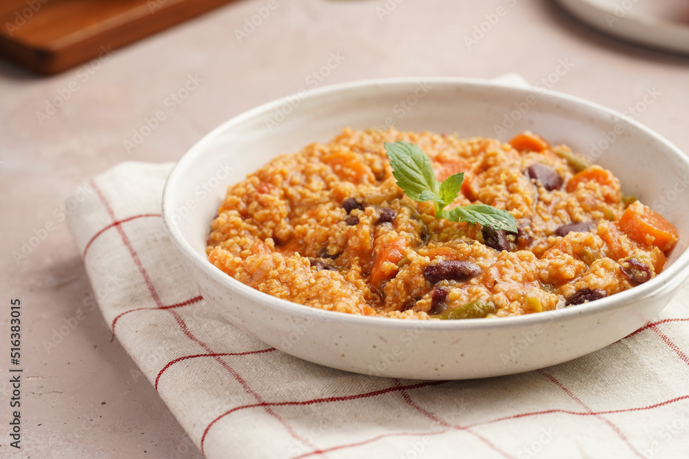 Grain dish - Millet with tomatoes, beans, carrots and spices, mint in a white bowl on a concrete round tray with checkered linen kitchen towel on purple background Grain dish - Millet with tomatoes, beans, carrots and spices, mint in a white bowl on a concrete round tray with checkered linen kitchen towel on purple background
