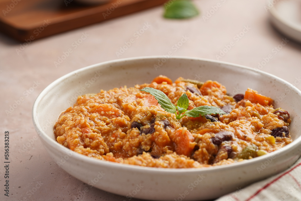 Grain dish - Millet with tomatoes, beans, carrots, bell pepper and spices, mint in a white bowl on a checkered linen kitchen towel on purple background Grain dish - Millet with tomatoes, beans, carrots, bell pepper and spices, mint in a white bowl on a checkered linen kitchen towel on purple background