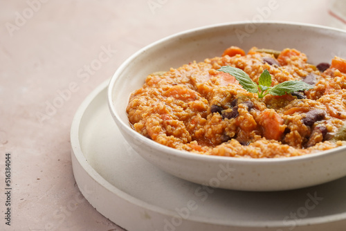 Grain dish - Millet with tomatoes, beans, carrots and spices, mint in a white bowl on a concrete round tray with checkered linen kitchen towel on purple background