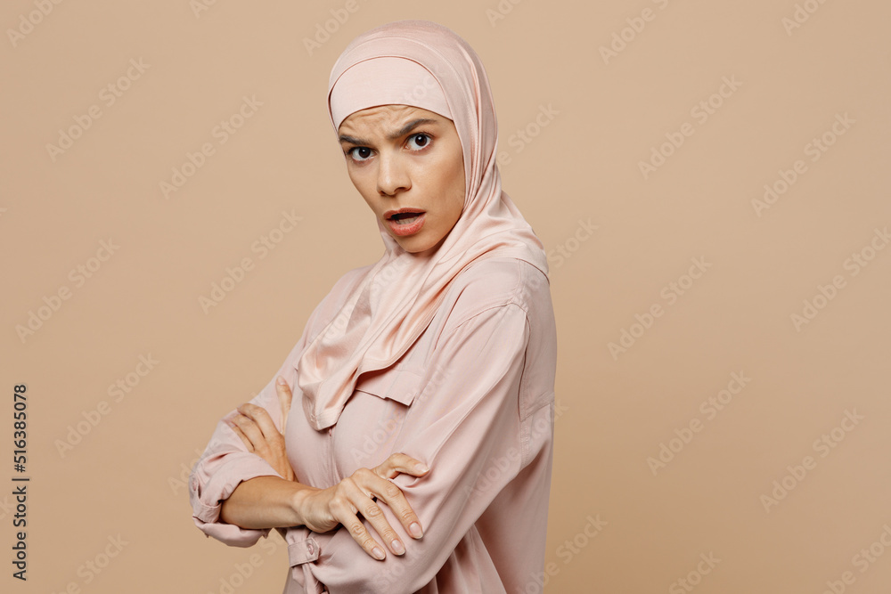Young sad arabian asian muslim woman she wearing abaya hijab pink clothes hold hands crossd folded isolated on plain pastel light beige background. People uae middle eastern islam religious concept.