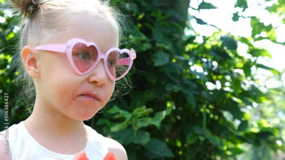 A little girl is eating a watermelon on the green grass in the garden.Summer, vacation, picnic in nature. A little girl is eating a watermelon on the green grass in the garden.Summer, vacation, picnic in nature.