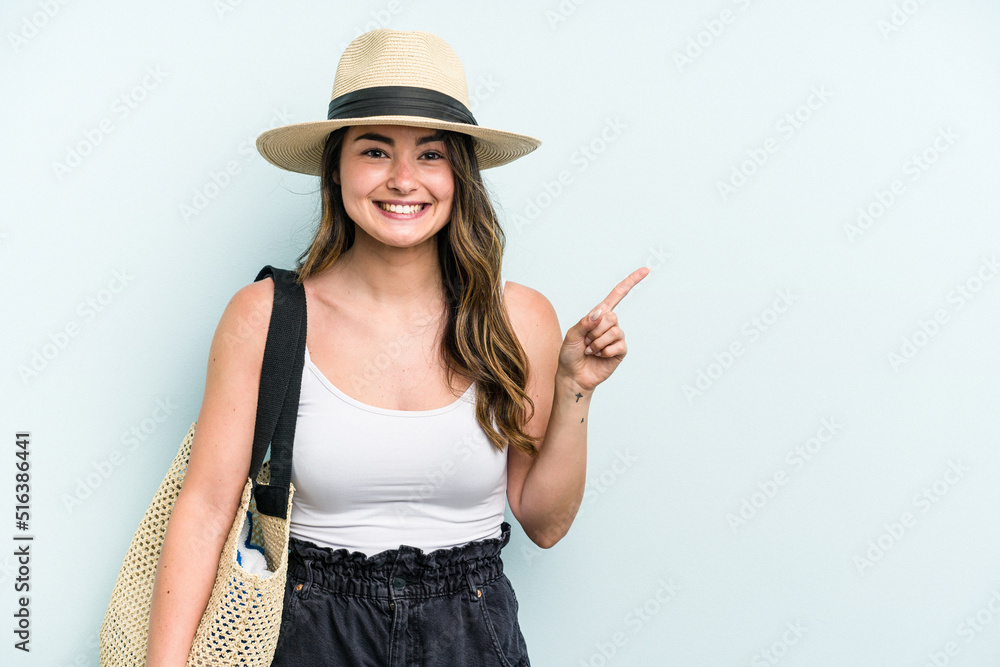 Young caucasian woman holding beach bag isolated on blue background smiling and pointing aside, showing something at blank space. Young caucasian woman holding beach bag isolated on blue background smiling and pointing aside, showing something at blank space.