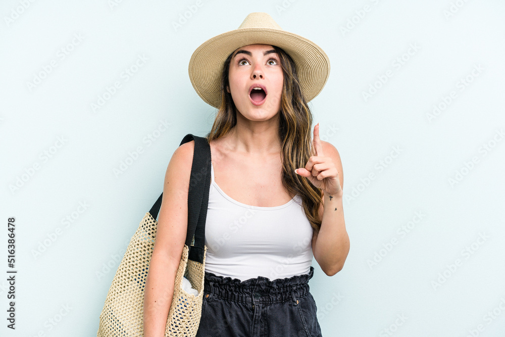 Young caucasian woman holding beach bag isolated on blue background pointing upside with opened mouth.