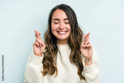 Fototapet Young caucasian woman isolated on blue background crossing fingers for having lu