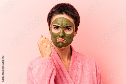 Young caucasian woman wearing a face mask isolated on pink background showing fist to camera, aggressive facial expression.