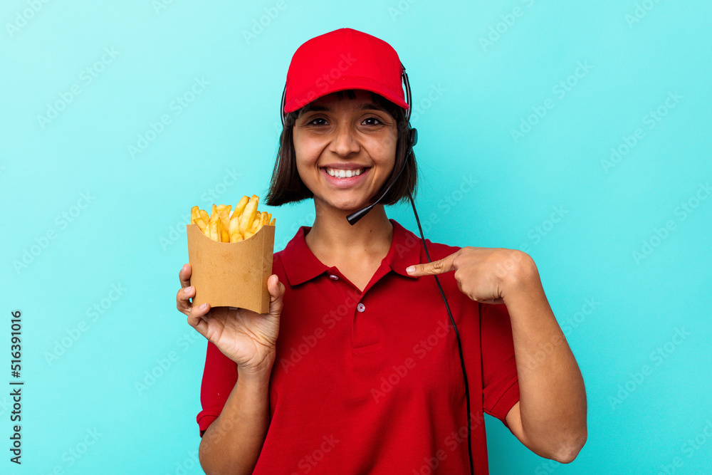 Young mixed race woman fast food restaurant worker holding fries isolated on blue background person pointing by hand to a shirt copy space, proud and confident Young mixed race woman fast food restaurant worker holding fries isolated on blue background person pointing by hand to a shirt copy space, proud and confident