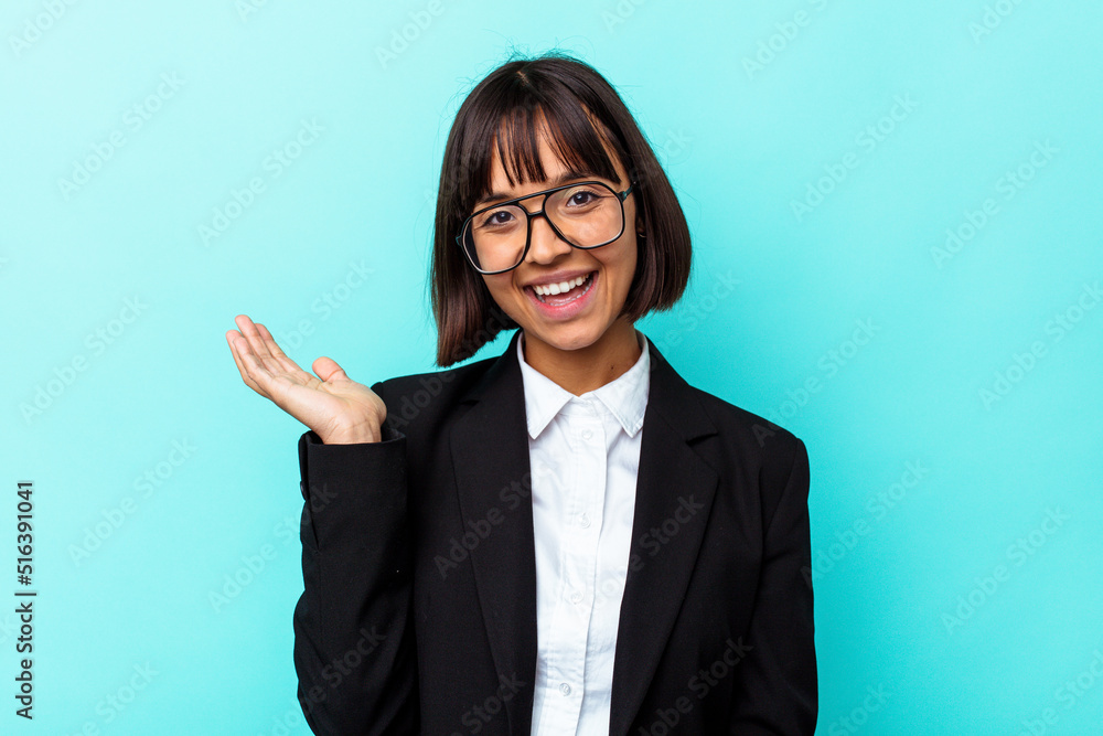 Young business mixed race woman isolated on blue background showing a copy space on a palm and holding another hand on waist. Young business mixed race woman isolated on blue background showing a copy space on a palm and holding another hand on waist.