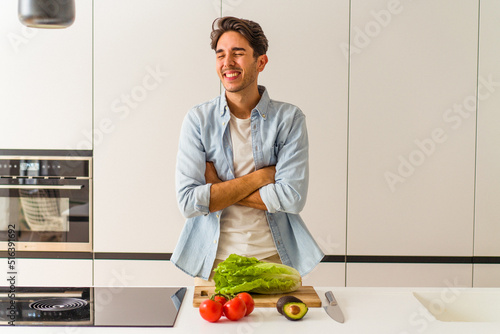 Young mixed race man preparing a salad for lunch laughing and having fun.