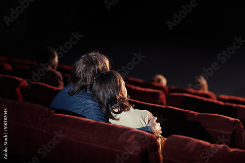 Rear view of affectionate couple embracing while watching movie on comfortable seats in cinema