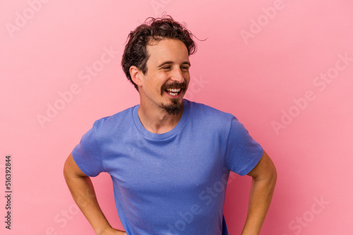 Young caucasian man isolated on pink background laughs happily and has fun keeping hands on stomach.