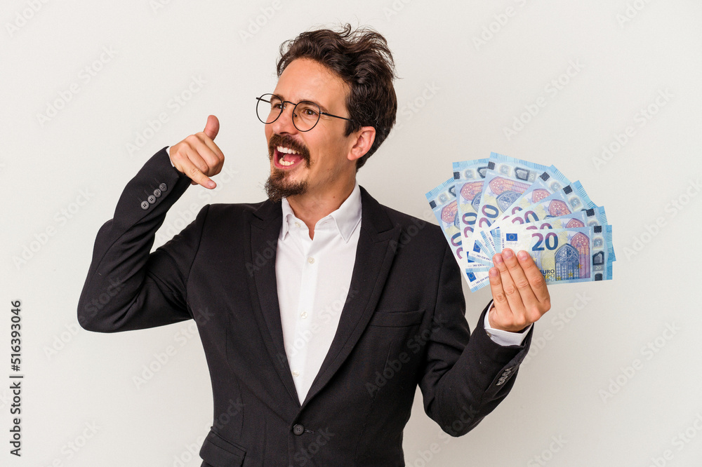 Young caucasian man holding banknotes isolated on white background showing a mobile phone call gesture with fingers. Young caucasian man holding banknotes isolated on white background showing a mobile phone call gesture with fingers.
