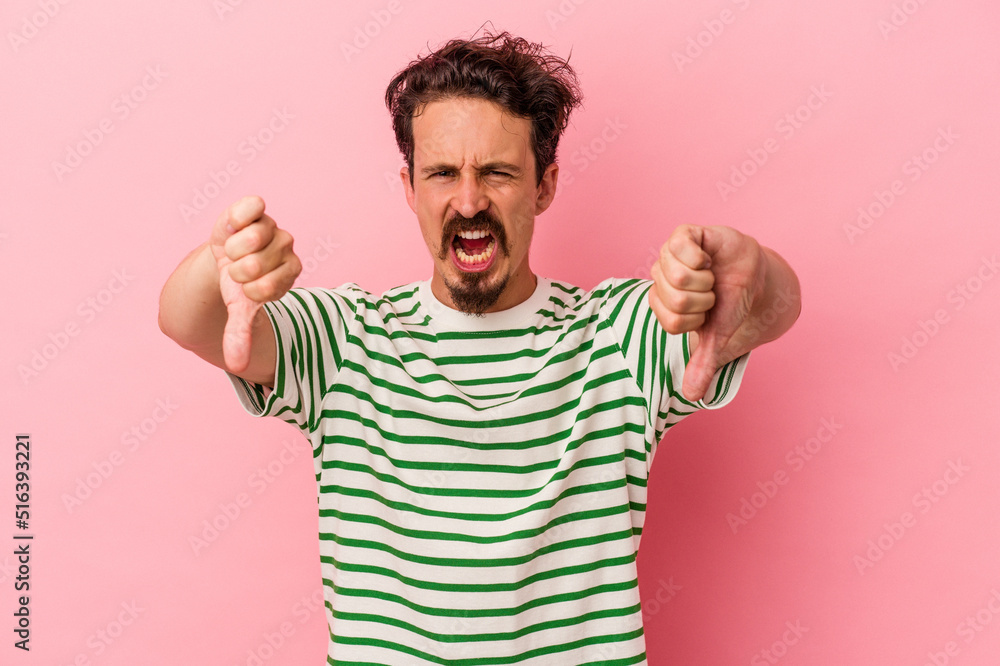 Fototapeta premium Young caucasian man isolated on pink background showing thumb down and expressing dislike.