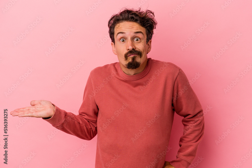 Young caucasian man isolated on pink background showing a copy space on a palm and holding another hand on waist. Young caucasian man isolated on pink background showing a copy space on a palm and holding another hand on waist.