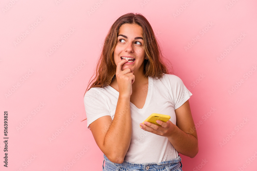 Young caucasian woman using mobile phone isolated on pink background relaxed thinking about something looking at a copy space. Young caucasian woman using mobile phone isolated on pink background relaxed thinking about something looking at a copy space.