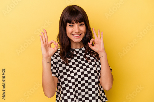 Young caucasian woman isolated on yellow background cheerful and confident showing ok gesture.