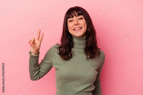 Young caucasian woman isolated on pink background showing victory sign and smiling broadly.