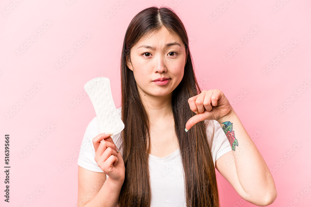 Young asian woman holding sanitary napkin isolated on pink background showing a dislike gesture, thumbs down. Disagreement concept. Young asian woman holding sanitary napkin isolated on pink background showing a dislike gesture, thumbs down. Disagreement concept.