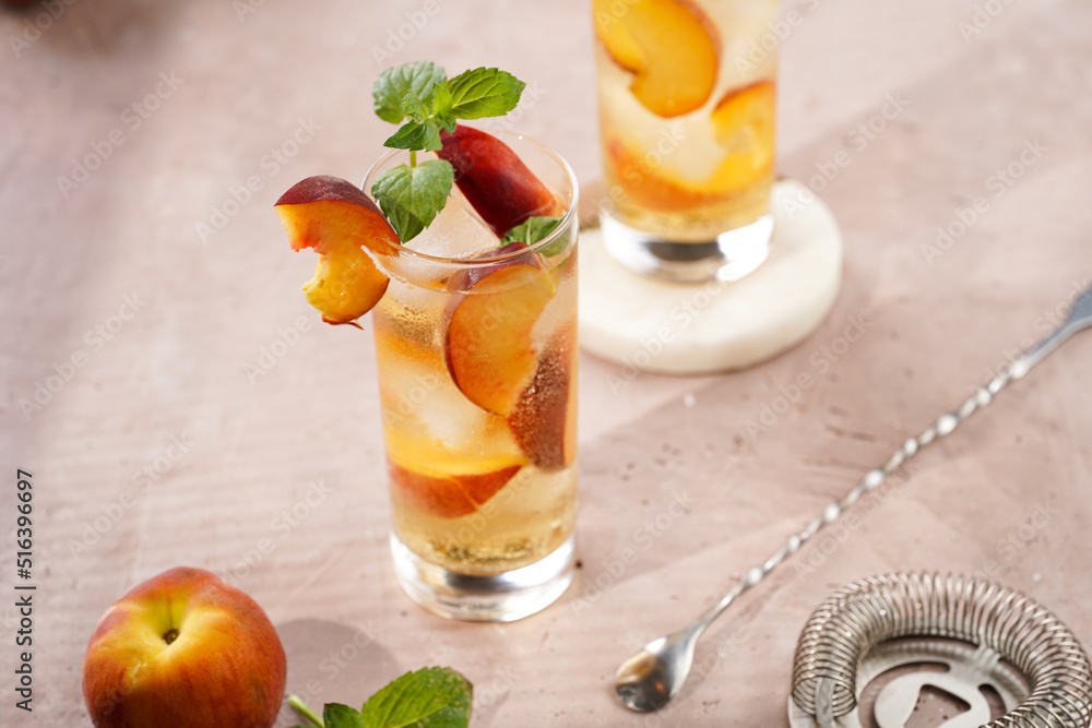 Fototapeta premium Two glasses with refreshing summer cocktail with ice cubes, peach slices and fresh mint on pale purple background