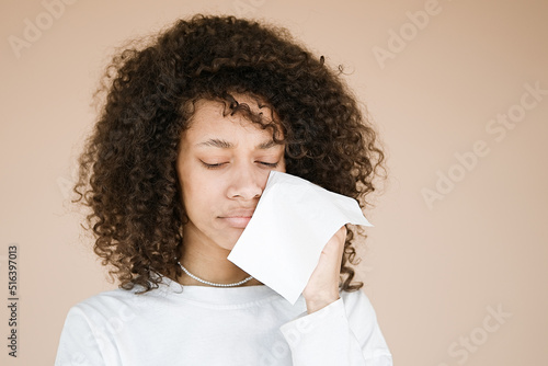 Tableau sur toile Upset doleful young african american woman sobs and cries from despair wipes tears away with a tissue isolated over beige background with copy space for your advertising content