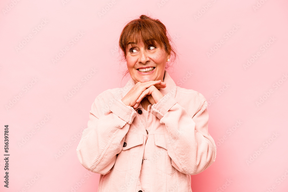 Middle age caucasian woman isolated on pink background keeps hands under chin, is looking happily aside. Middle age caucasian woman isolated on pink background keeps hands under chin, is looking happily aside.