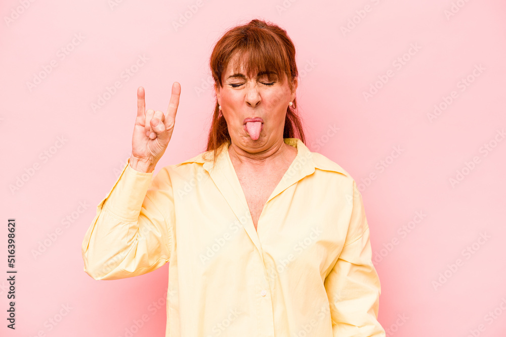 Middle age caucasian woman isolated on pink background showing rock gesture with fingers Middle age caucasian woman isolated on pink background showing rock gesture with fingers