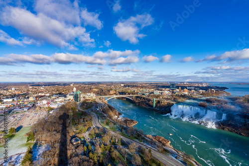 Niagara Falls City, Ontario, Canada - December 19 2021 : Overlooking the Niagara River Rainbow Bridge and American Falls in a sunny day.