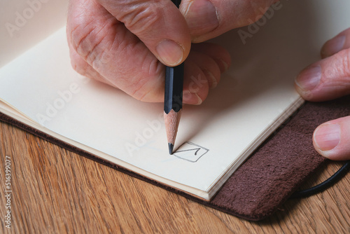 Elderly woman's hands holding a pencil and puts a check mark on an empty page. Selective focus