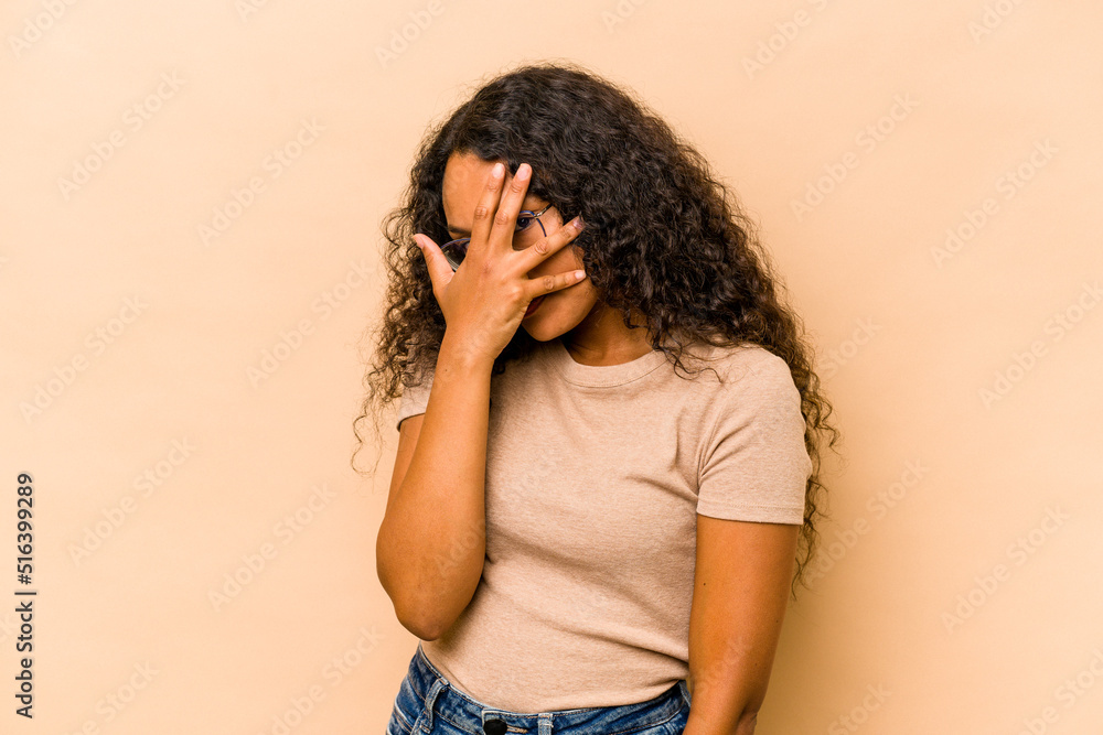 Young hispanic woman isolated on beige background blink at the camera through fingers, embarrassed covering face. Young hispanic woman isolated on beige background blink at the camera through fingers, embarrassed covering face.
