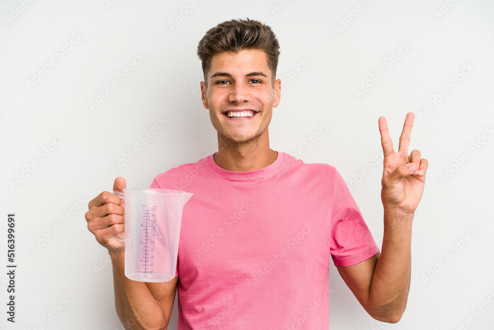 Young caucasian man holding measuring jug isolated on white background showing number two with fingers. Young caucasian man holding measuring jug isolated on white background showing number two with fingers.