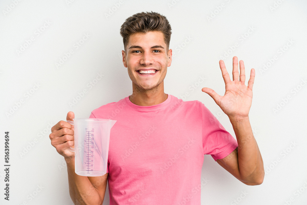 Young caucasian man holding measuring jug isolated on white background smiling cheerful showing number five with fingers.