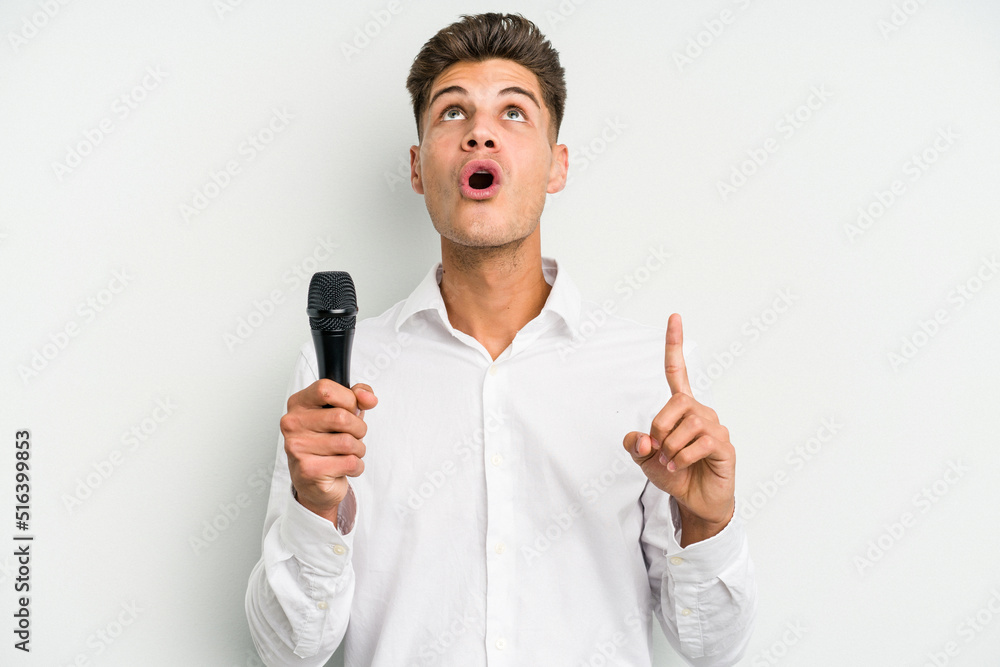 Young singer caucasian man isolated on white background pointing upside with opened mouth. Young singer caucasian man isolated on white background pointing upside with opened mouth.