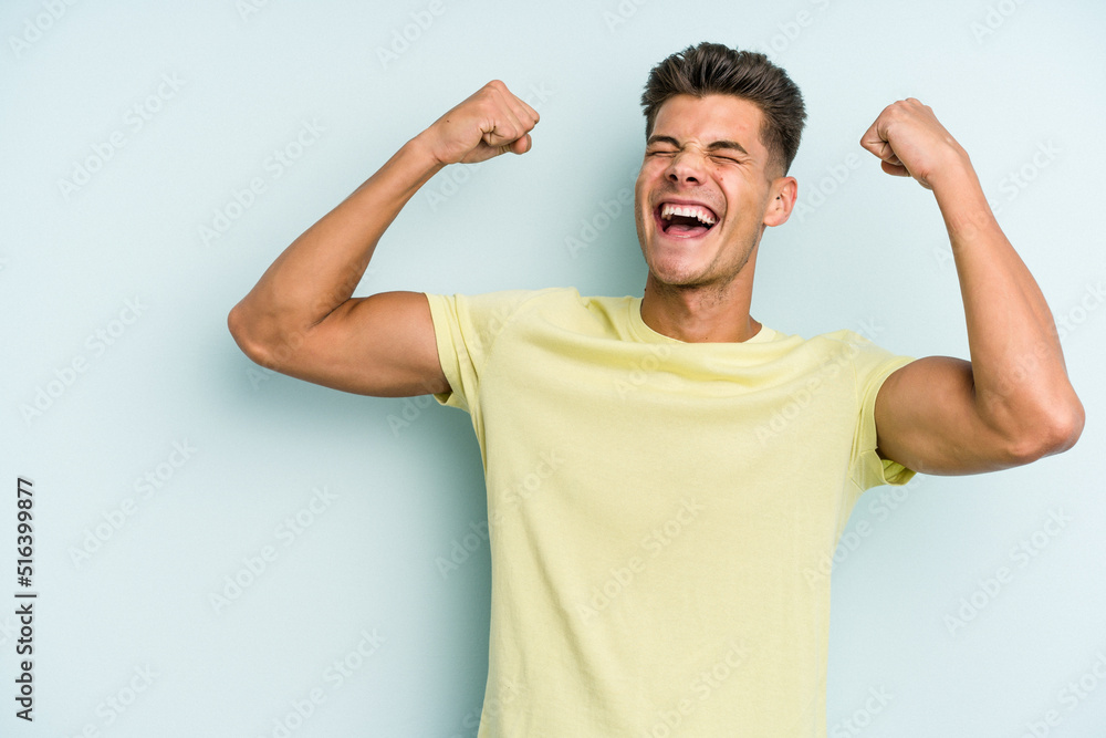 Young caucasian man isolated on blue background raising fist after a victory, winner concept. Young caucasian man isolated on blue background raising fist after a victory, winner concept.