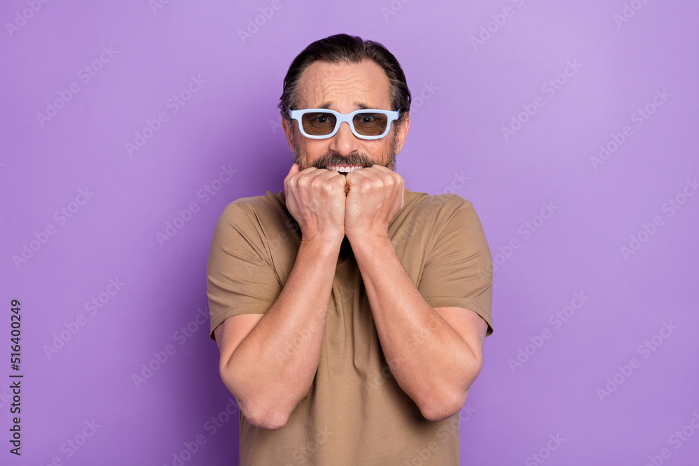 Obraz premium Photo of scared middle-aged man scared to watch 3d horror movie biting his knuckles isolated on violet color background