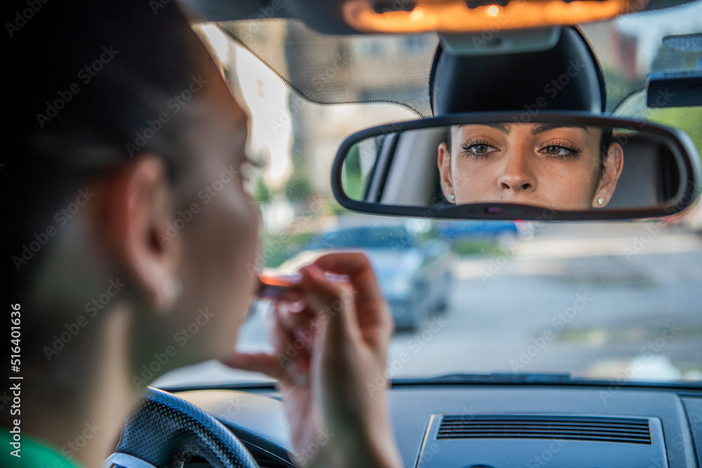 Beautiful young girl applying makeup while driving a car. Risky driving.
