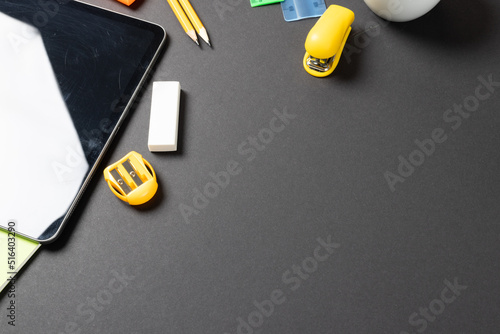 Imagine of various office supplies, pins, rulers, scissorson and tablet on black background