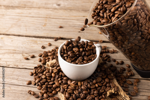 Image of white cup full of coffee beans on wooden background