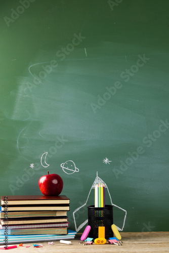 Image of school supplies, apple and notebook over drawings on black board