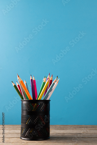 Image of cup of crayons on wooden table over blue background