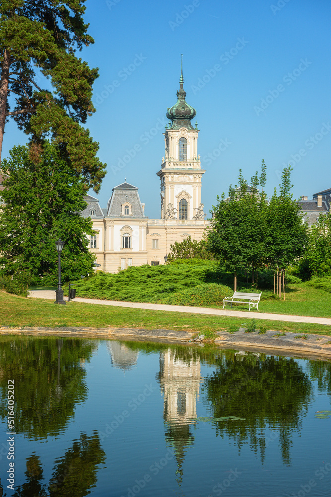 Festetics Palace with beautiful garden on sunny summer day, baroque architecture, Keszthely, Zala, Hungary. Outdoor travel background with flowers, green grass, blue sky and pond with reflection