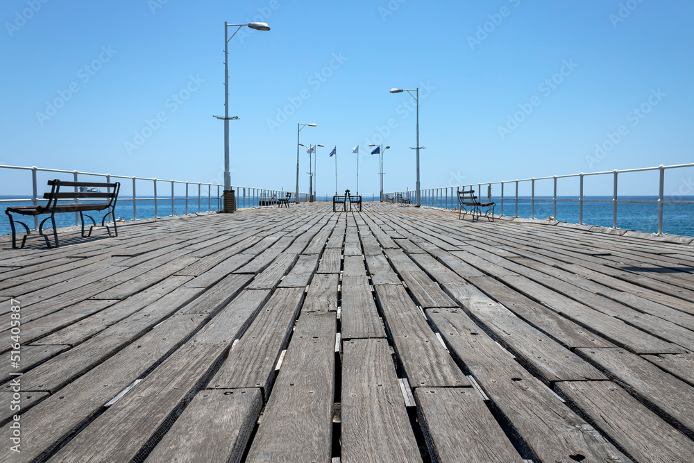 Empty wooden sea pier with benches, street lights and flags in Limassol Old port, Cyprus 